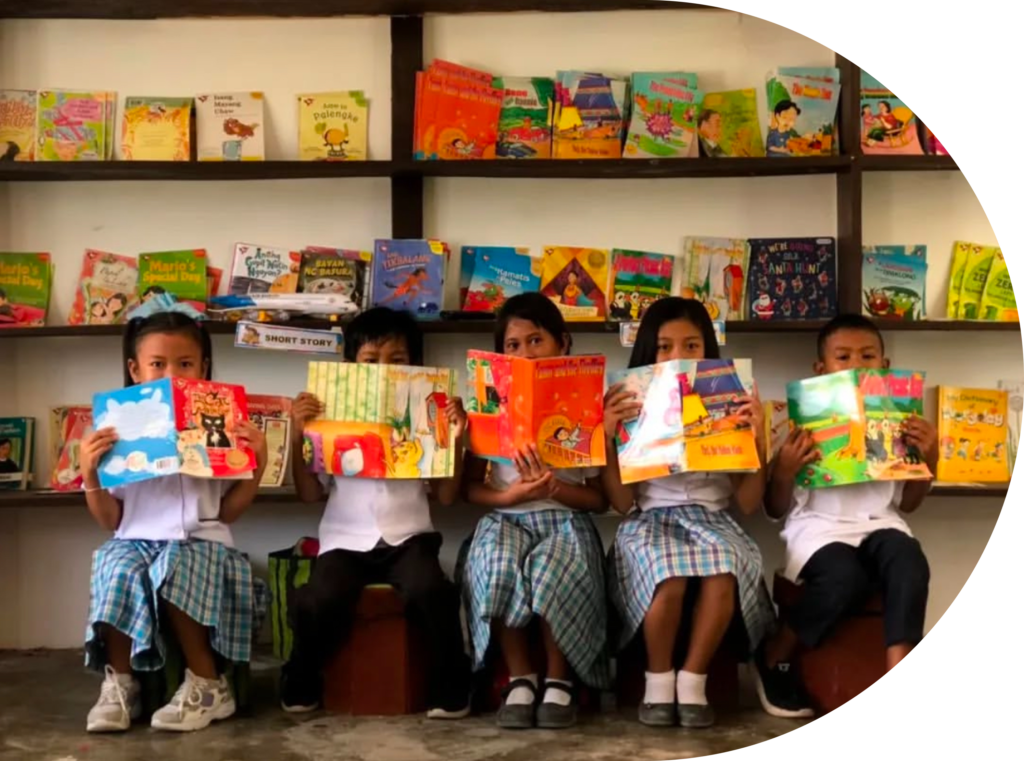 Five pupils holding open books in front of library bookshelves