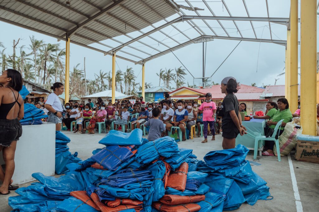 Relief tarpaulins stacked for distribution at a community gathering in Halian