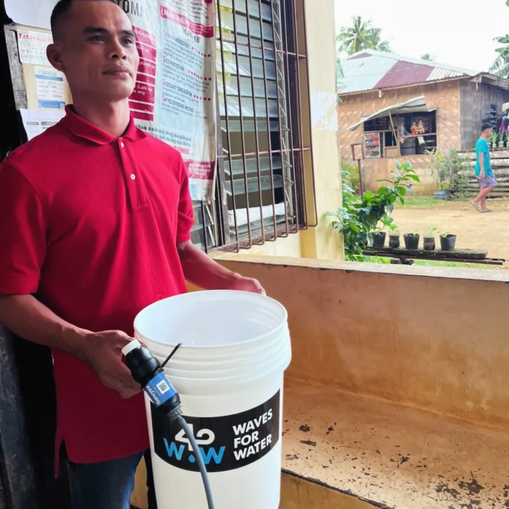 Community member holding a Waves for Water bucket with an attached filter